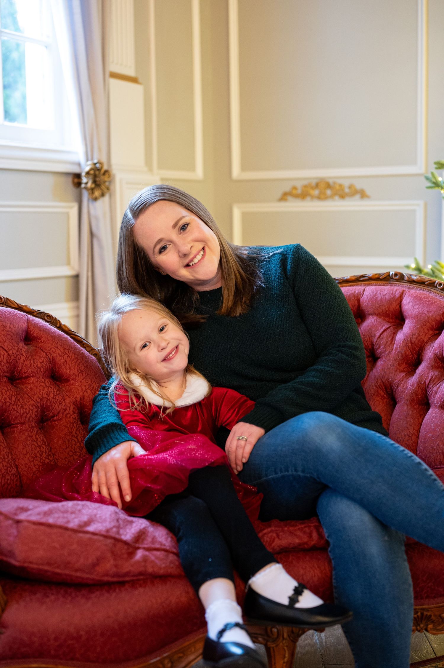 Two people share a joyful moment while relaxing on a burgundy velvet couch in a bright room. Family session. Portrait photography. Oregon.