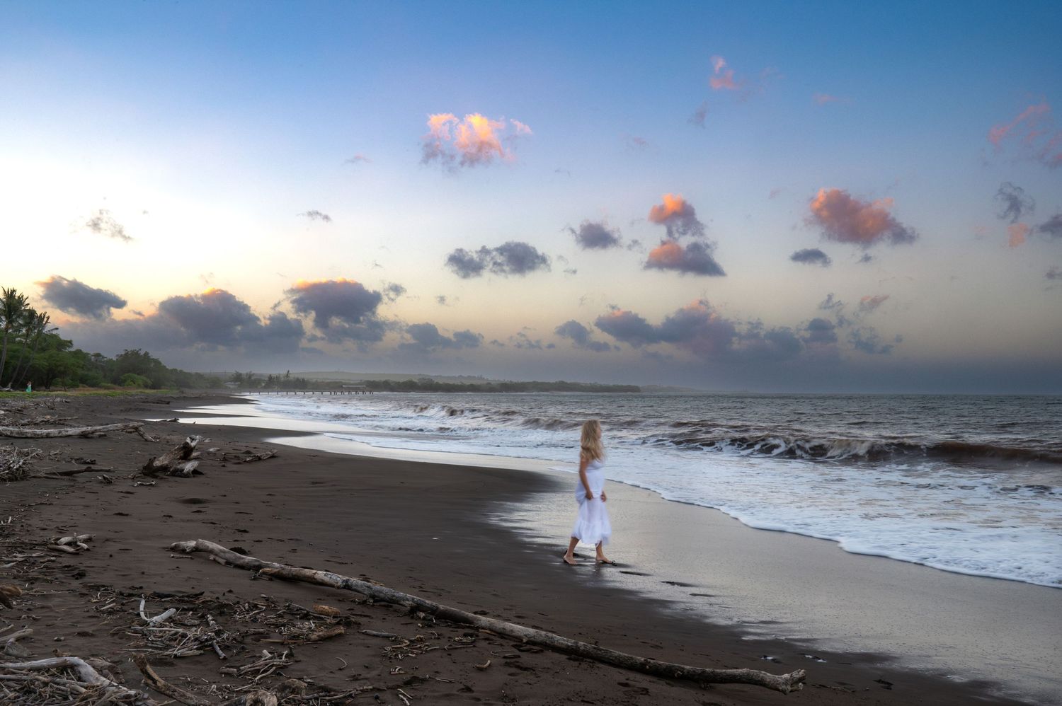 Solitary figure walking along a beach shoreline during golden hour.