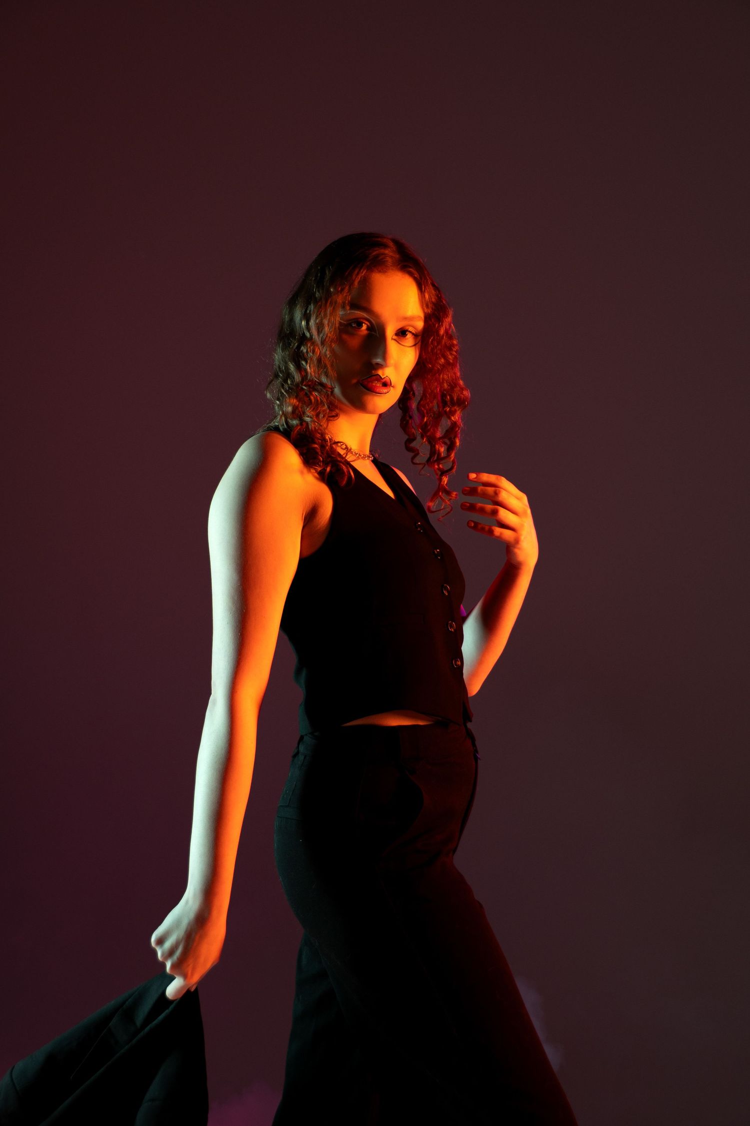 Fashion model in black two-piece outfit poses against dark background with red lighting. Creative portfolio. Studio. Portrait photography. O
