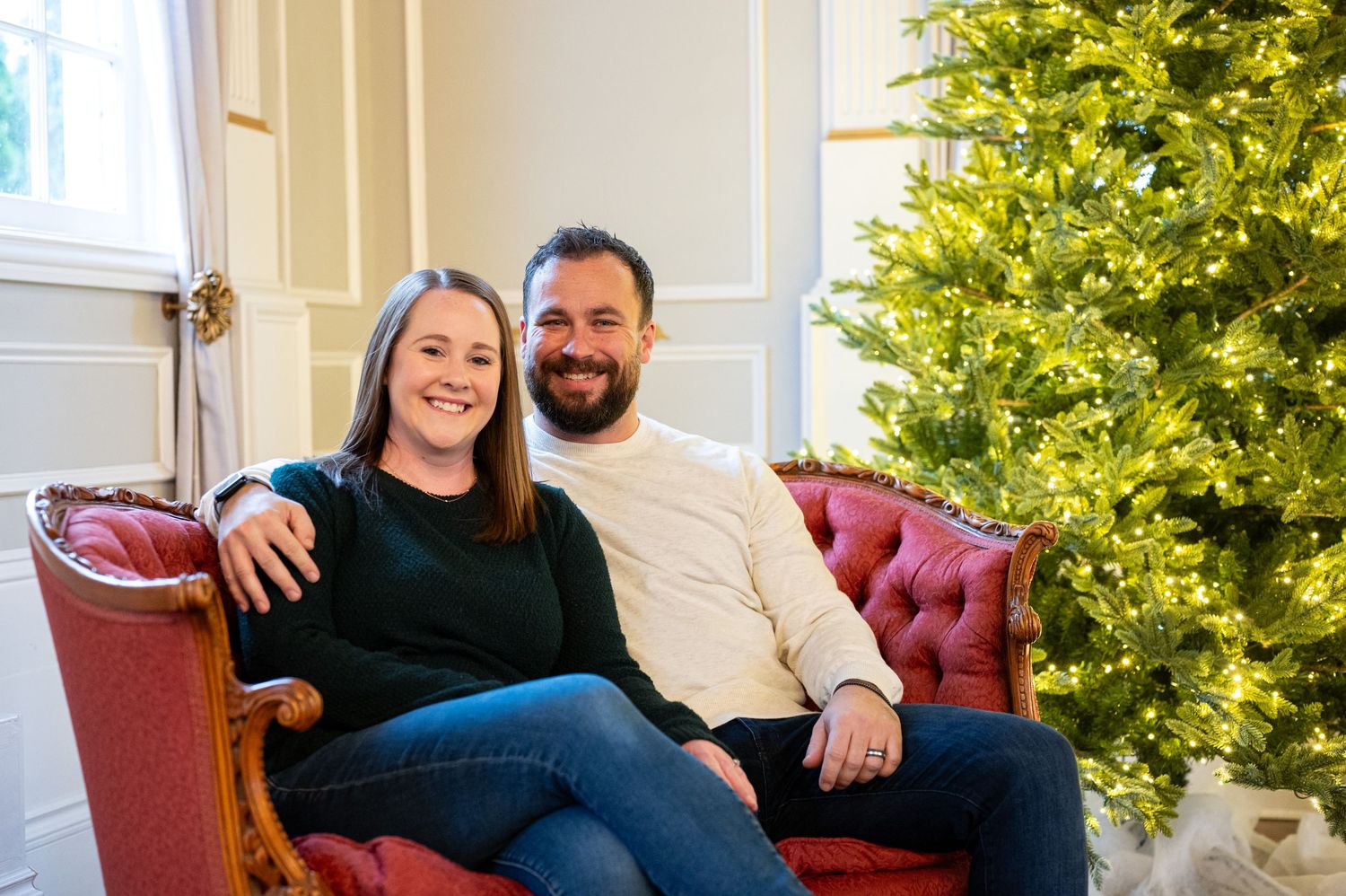 A couple relaxes on a vintage sofa during their holiday photo session with festive lights behind them. Family session. Portrait photography.