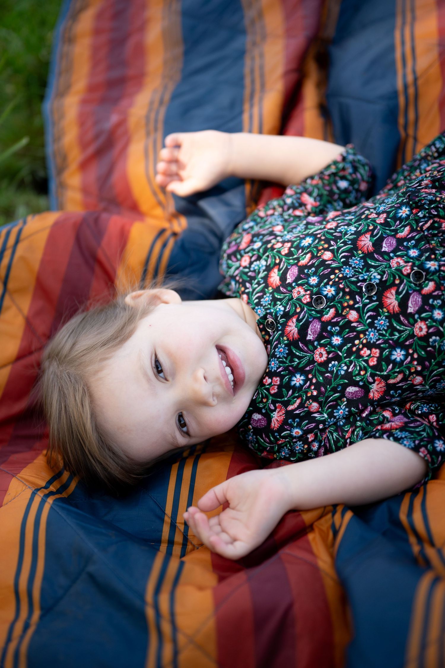 Person lying on striped blanket outdoors wearing floral dress in warm sunlight.
