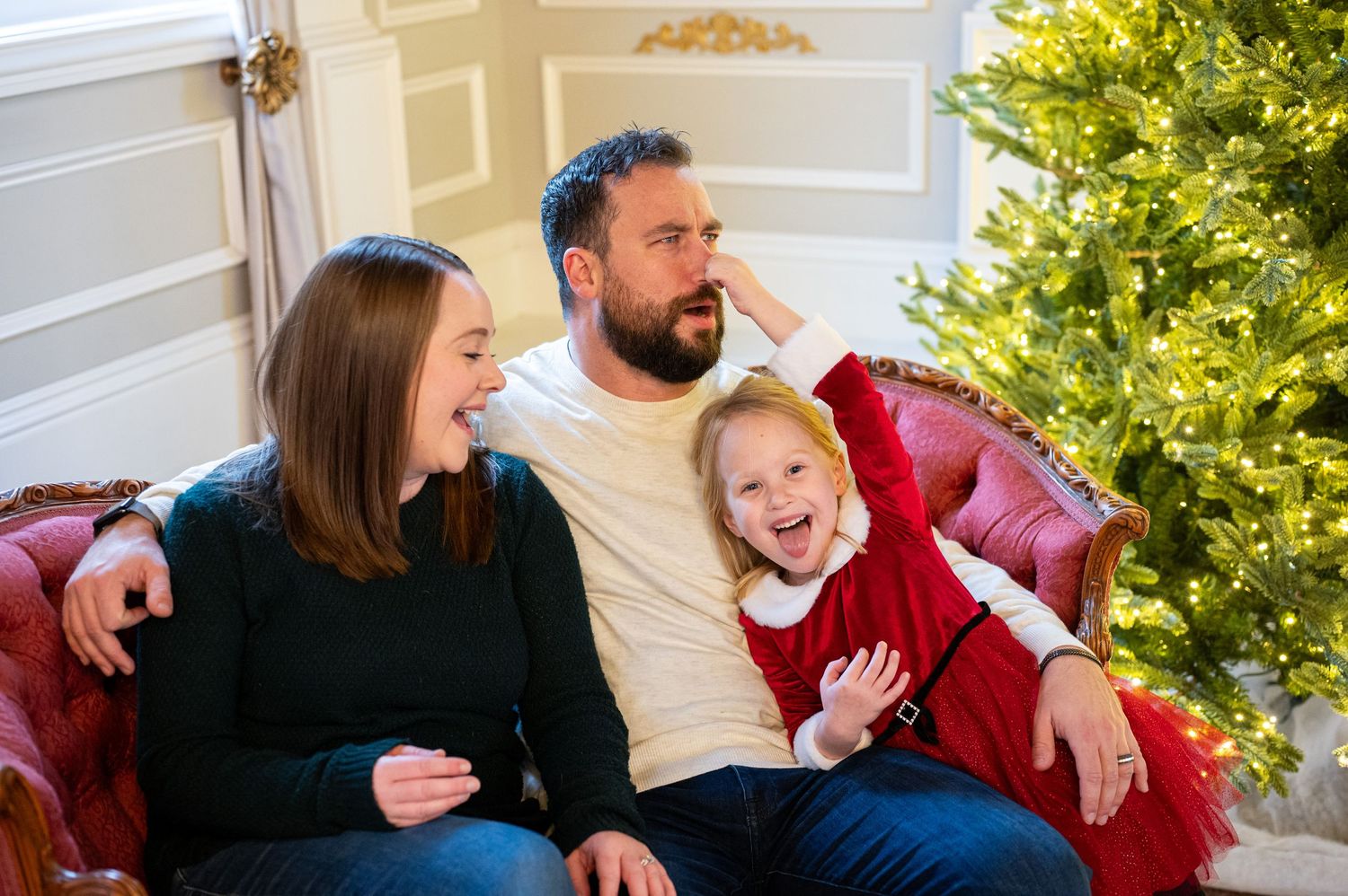 Family sharing a joyful moment on red couch near Christmas tree indoors. Family session. Portrait photography. Oregon.