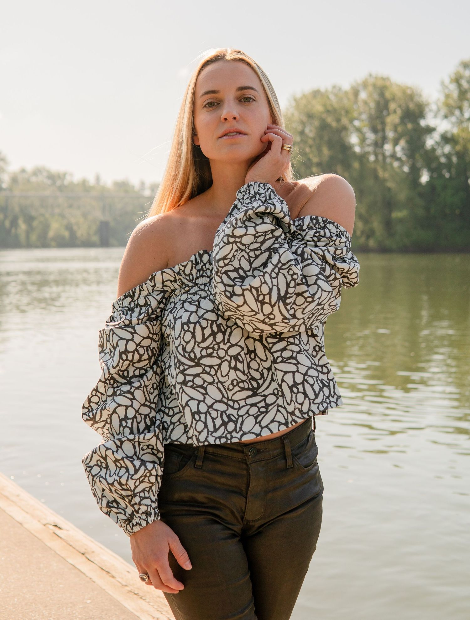 Outdoor portraits by a lake wearing patterned off-shoulder top and dark pants. Self portrait. The Option Agency.