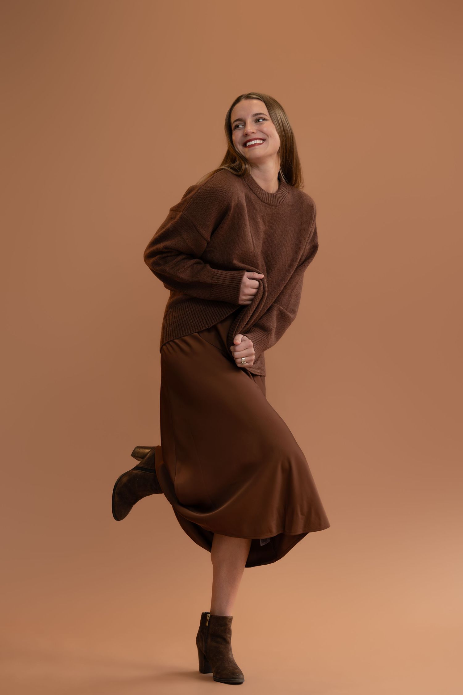 Model in oversized brown sweater dress striking dynamic poses against warm backdrop.