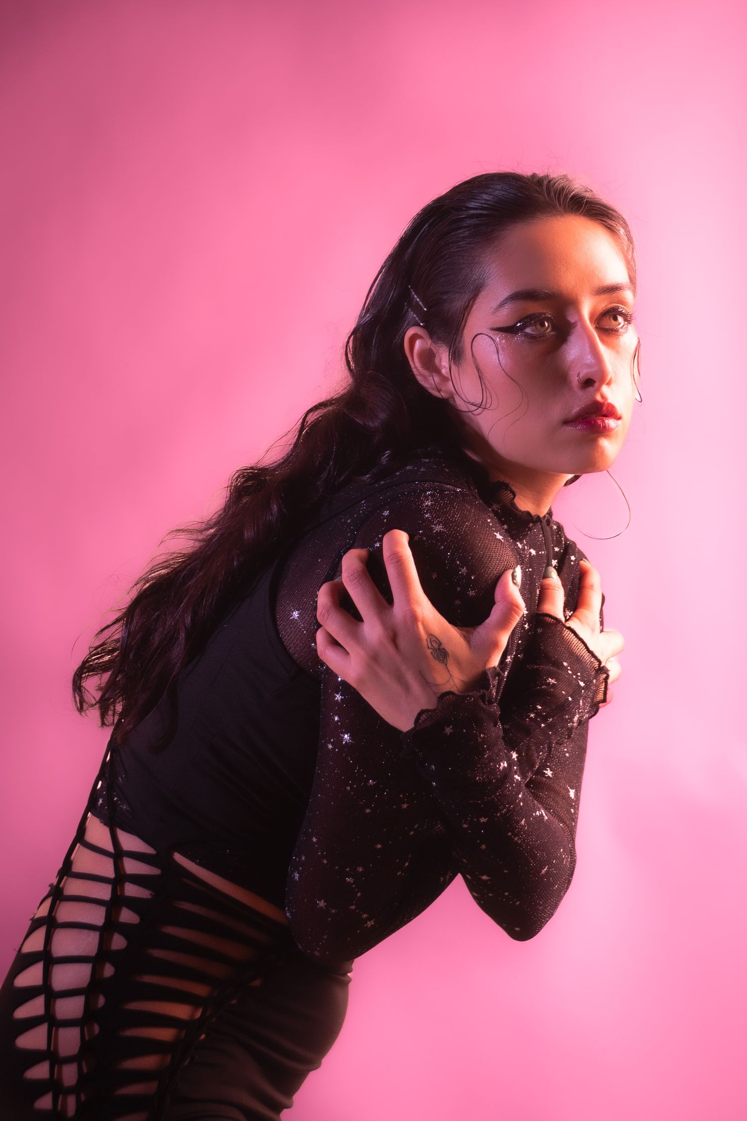 Fashion model in sparkly black bodysuit poses dramatically against pink backdrop with moody lighting. Creative portfolio. Studio. Portrait p