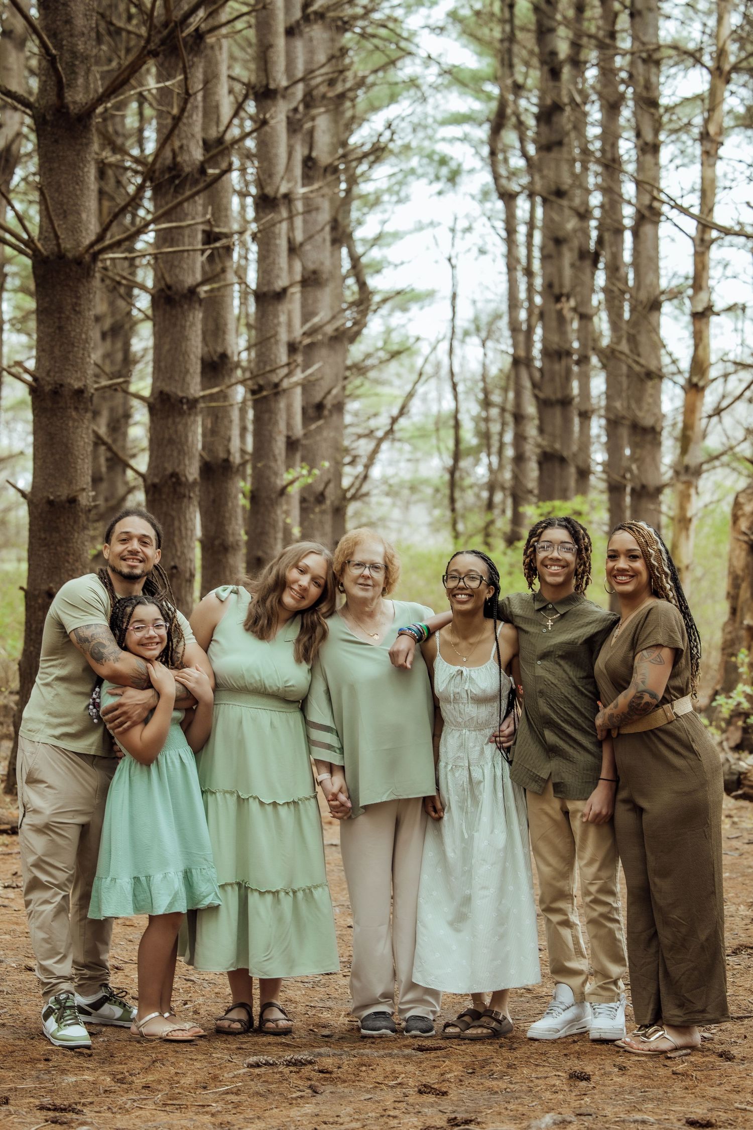 Extended multigenerational family posing together in a pine forest wearing coordinated earth-tone outfits.