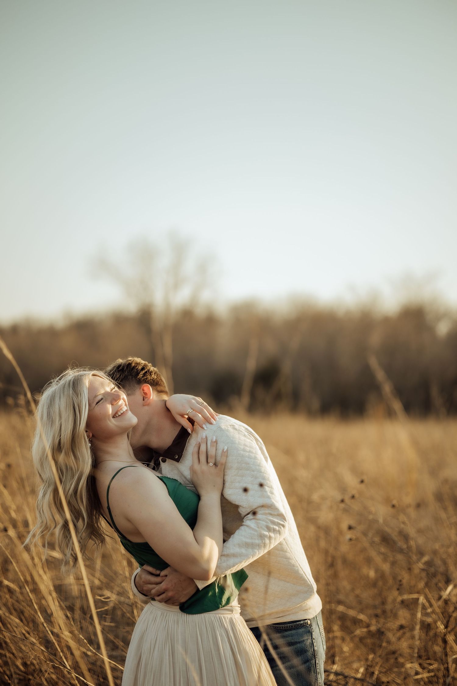 Couple embracing and kissing in a golden dry grass field under a clear open sky.