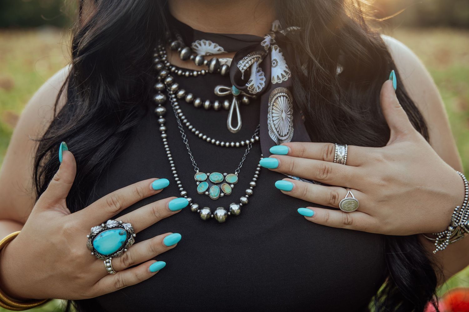 Close-up of layered turquoise and silver statement necklaces with turquoise nail polish and rings.