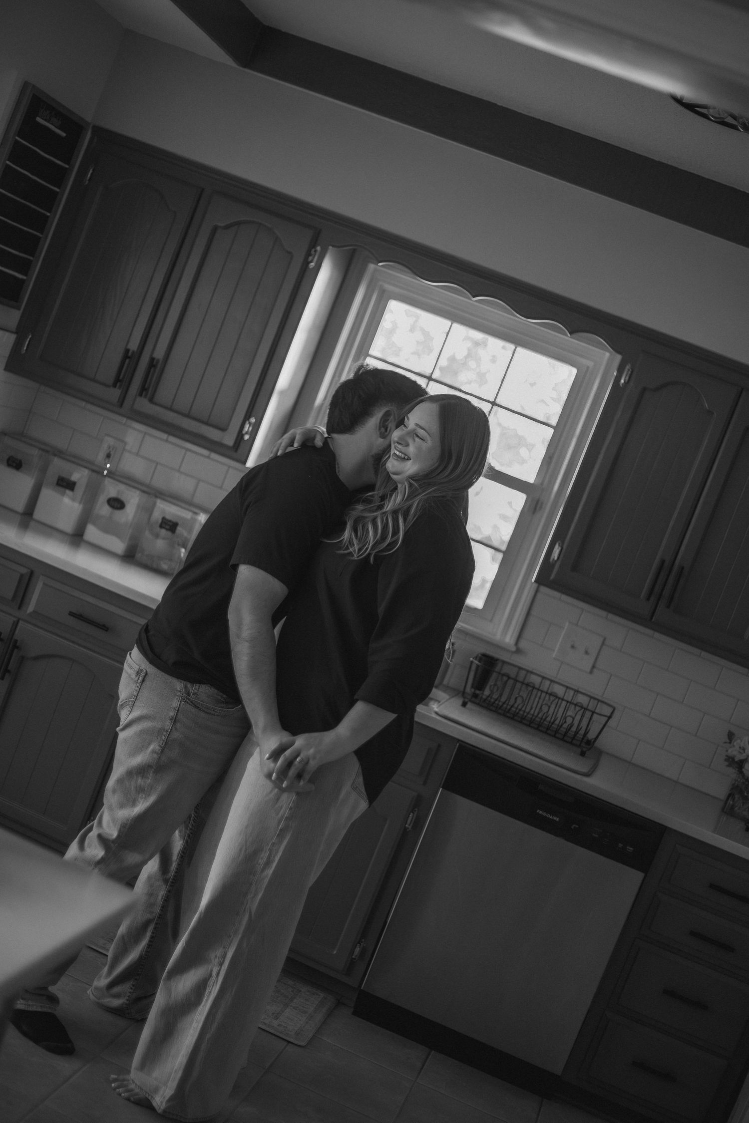 Black and white photo of couple sharing a tender kiss in their kitchen during an in-home engagement session.