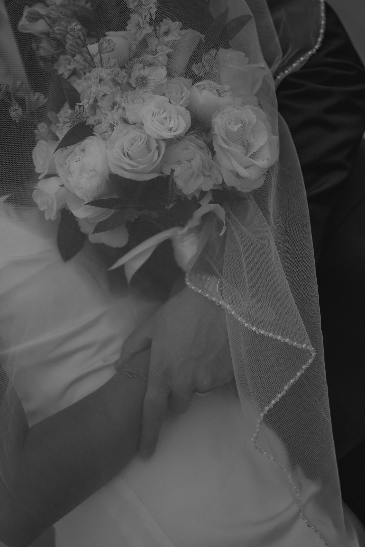 Black and white close-up of bride holding white rose bouquet with pearl-trimmed veil.
