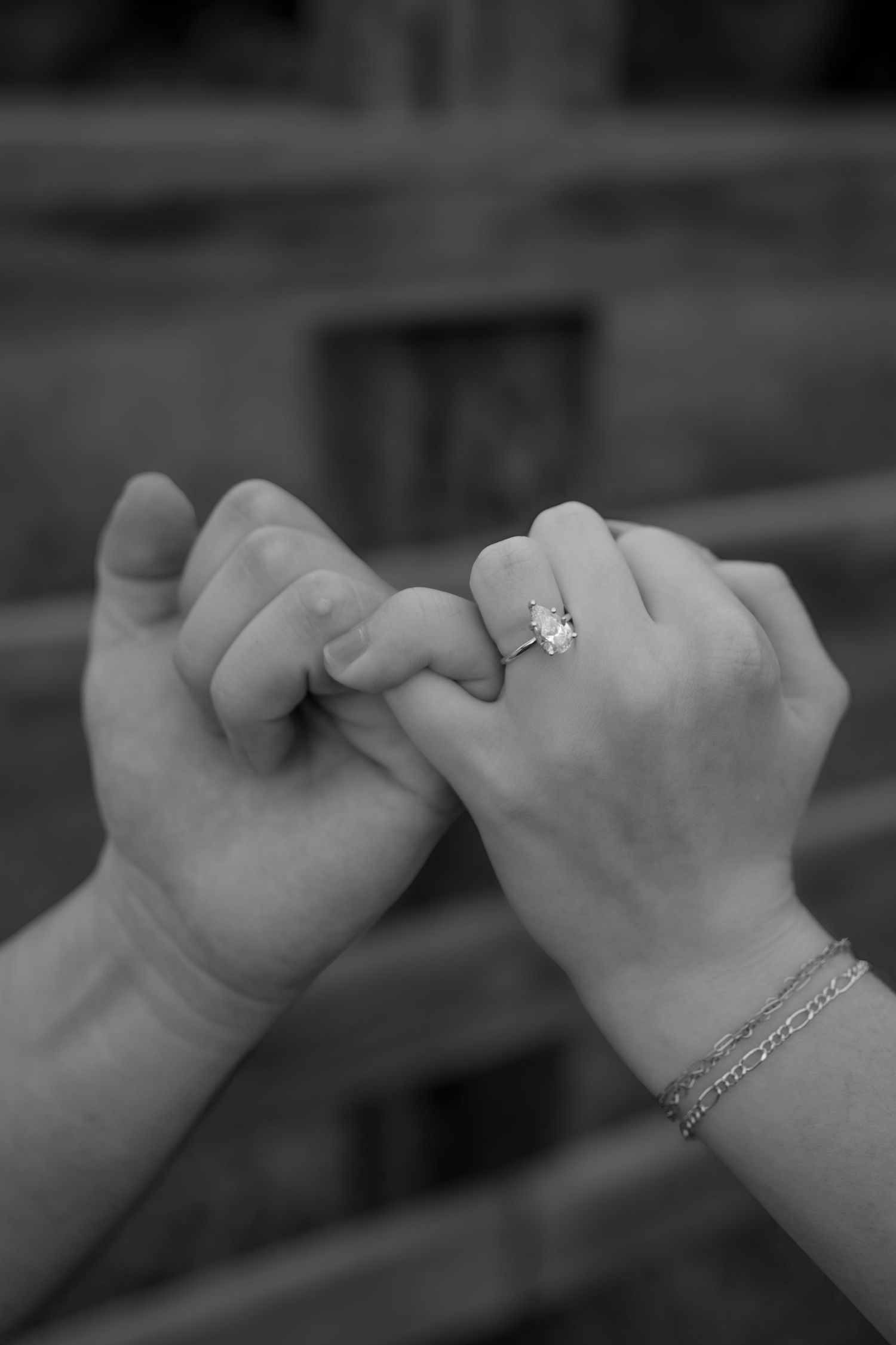 A close-up black and white photo of two hands interlocked, featuring a diamond engagement ring.