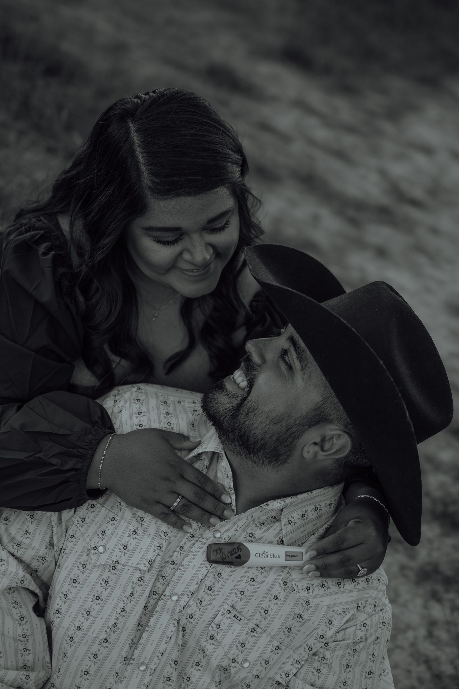 Black and white photo of a happy couple sharing a pregnancy test reveal in an outdoor setting.