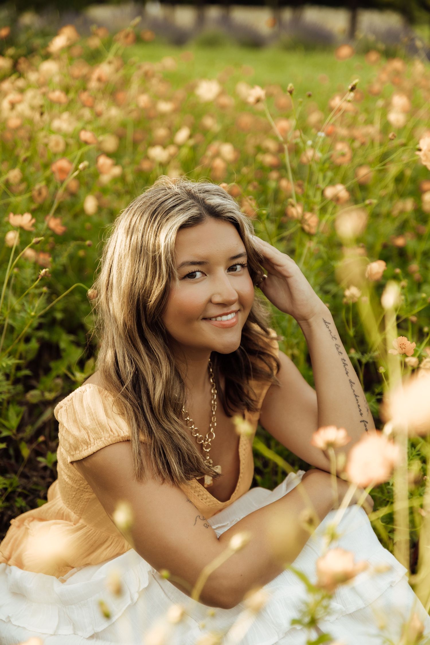 Young woman in yellow dress smiling among pink wildflowers in a sunny garden field.