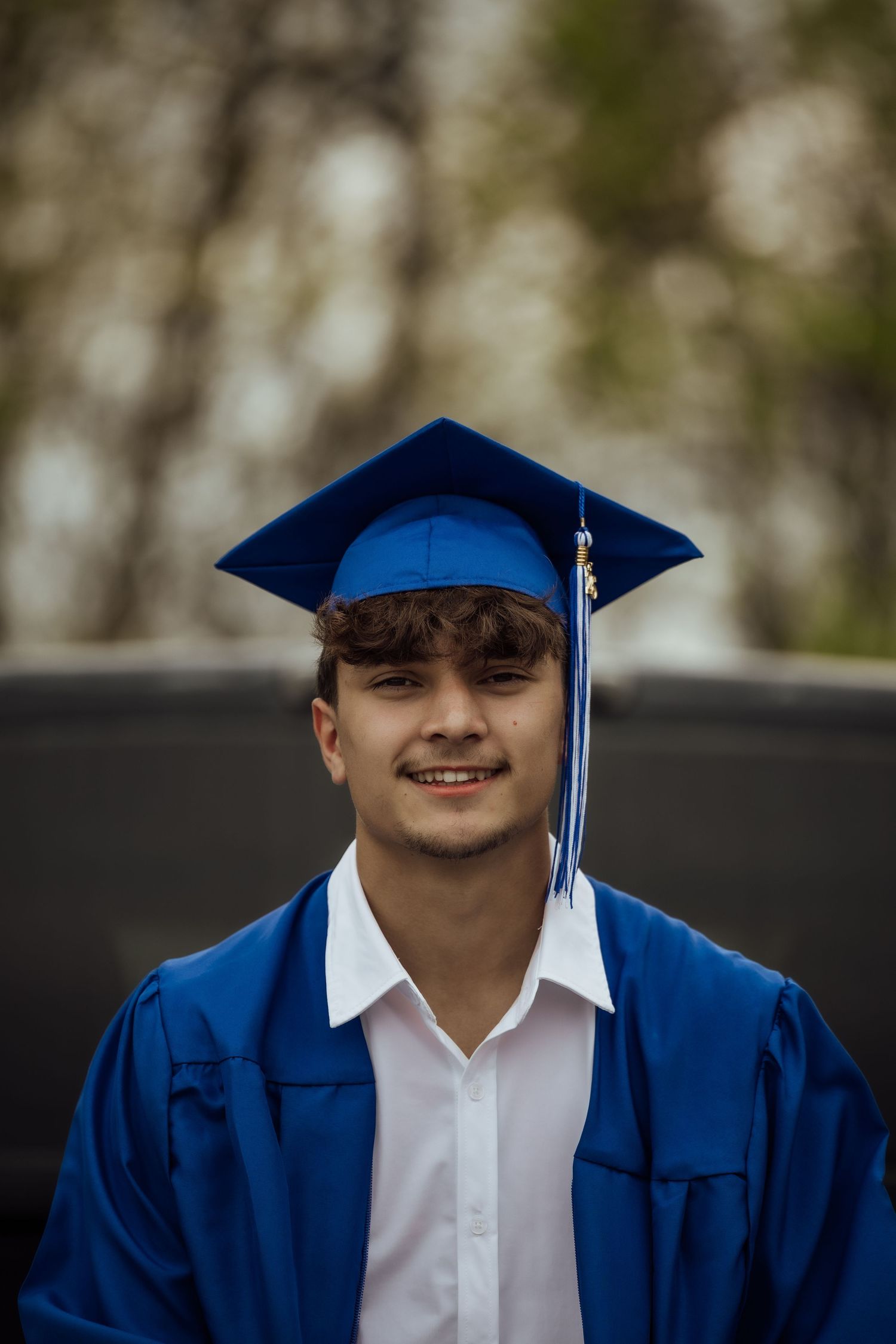 Smiling young man in blue graduation cap and gown poses for senior portrait.