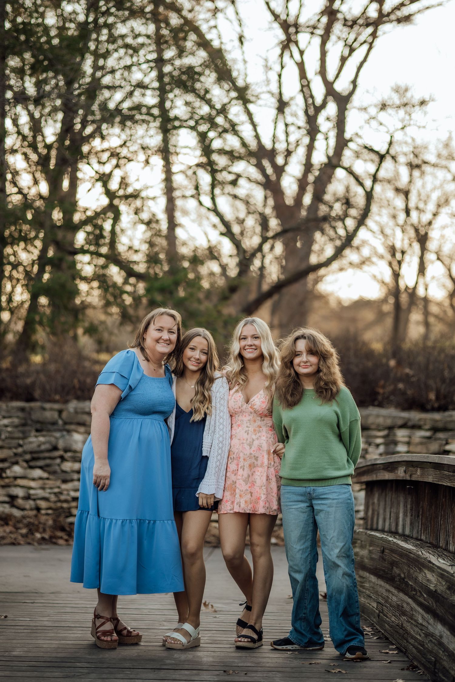 Mother and three teenage daughters posing on a wooden bridge during a golden hour family photo session.