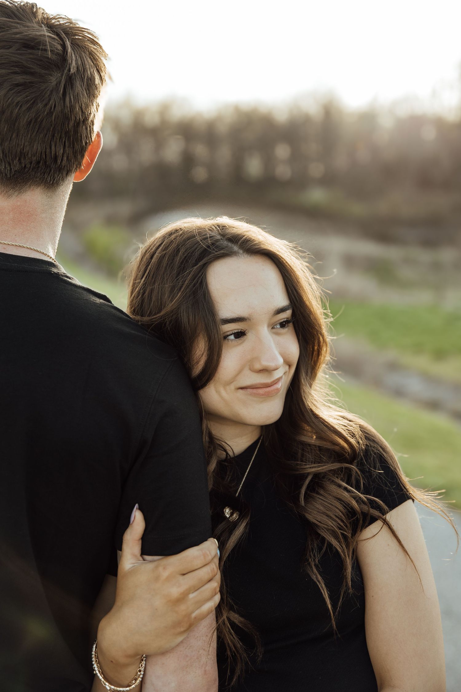 Young woman smiling warmly while resting her head against her partner's chest in a golden hour photo.
