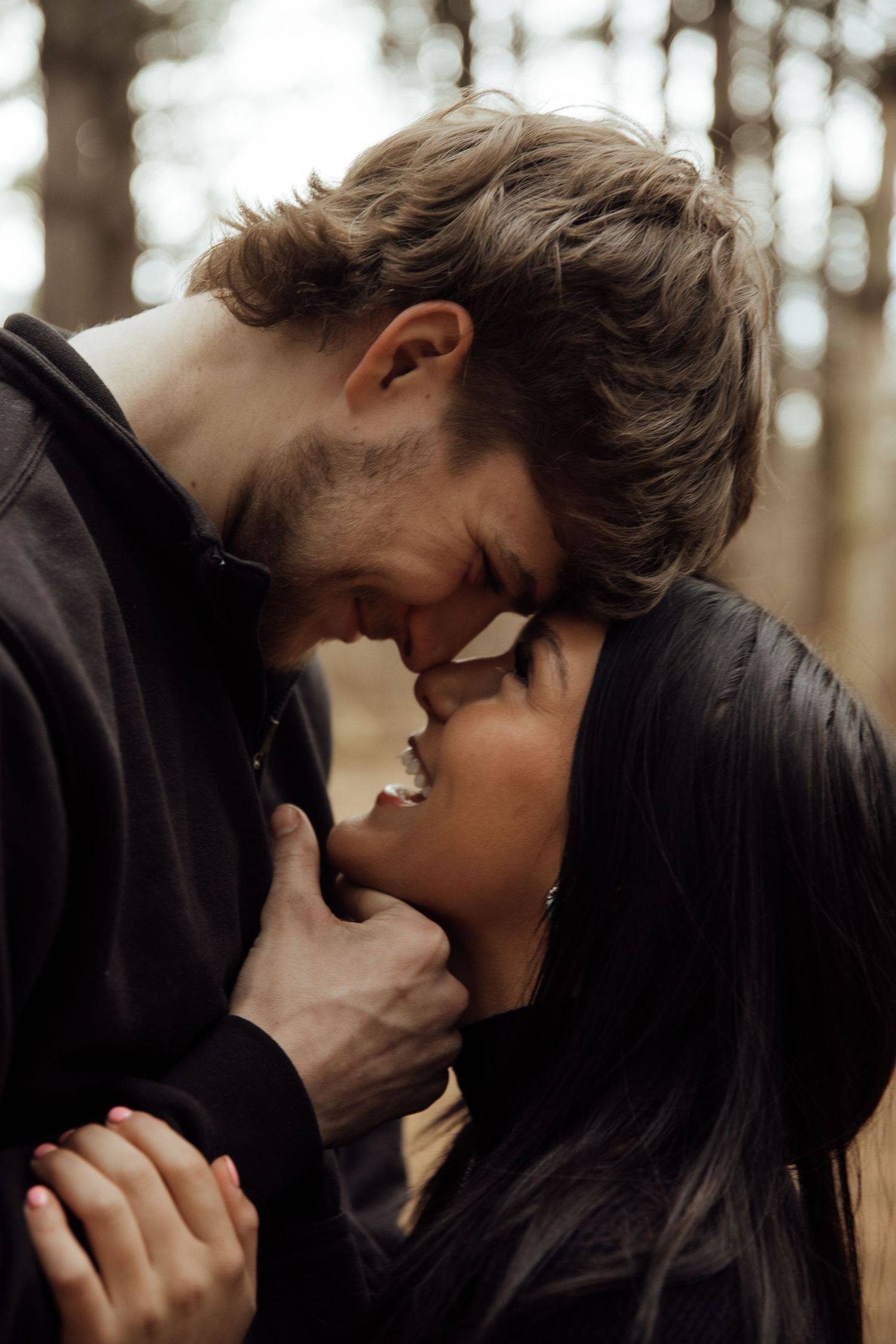 Romantic couple sharing an intimate almost-kiss moment together in a softly lit forest setting.