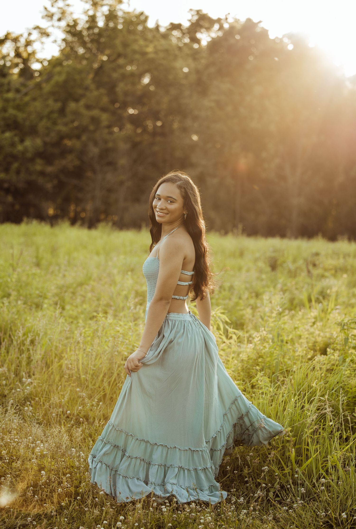 Young woman in mint ruffle maxi skirt posing in sunlit green meadow at golden hour.