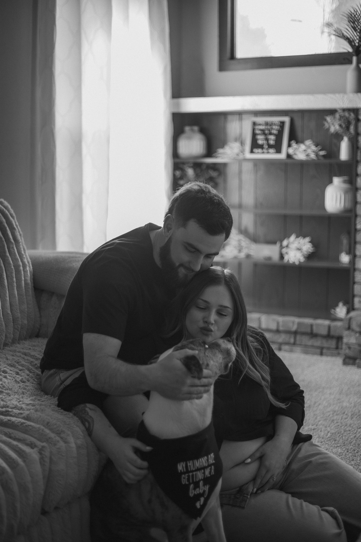 Black and white photo of loving couple cuddling their French bulldog on couch in cozy living room.