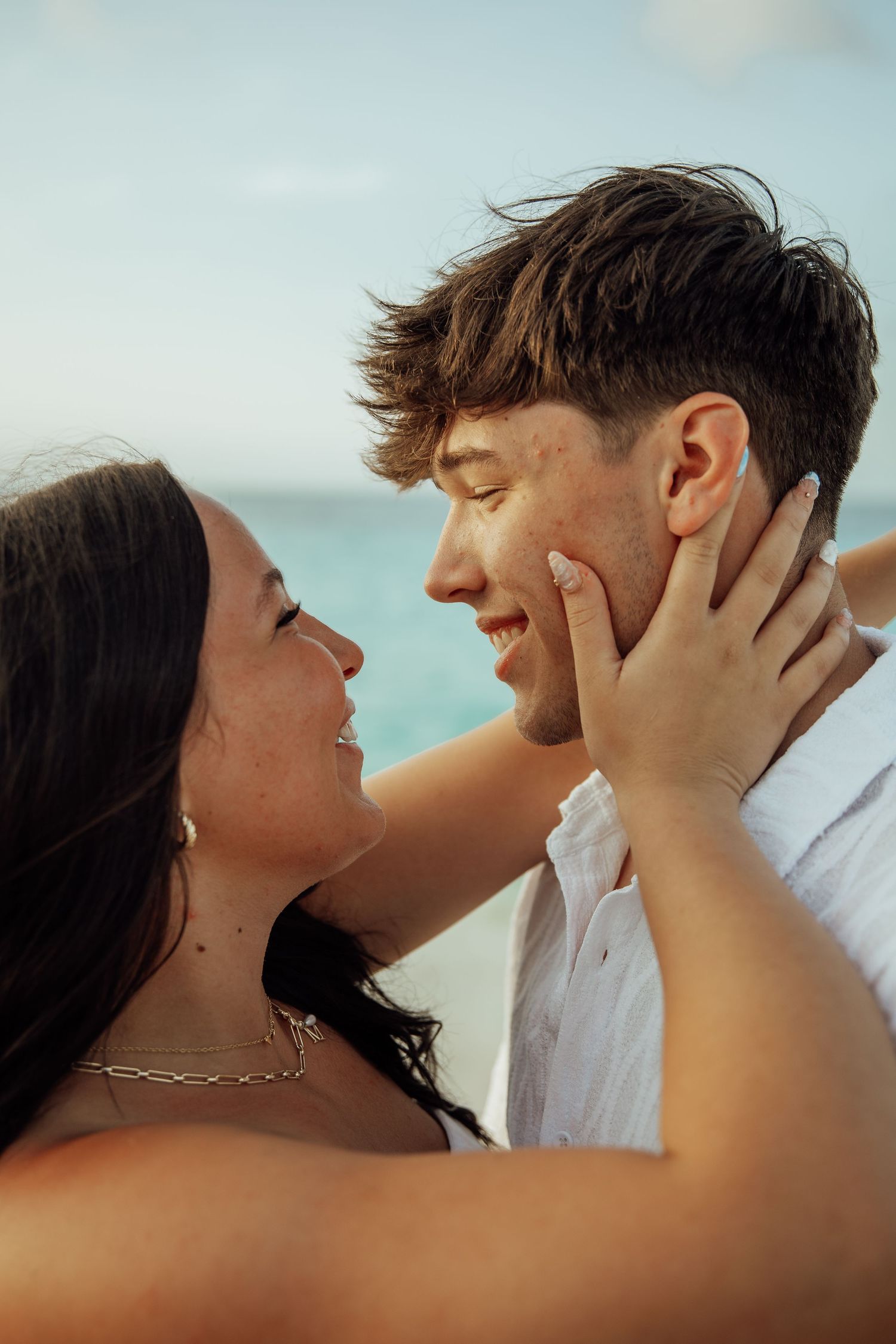 Couple sharing a romantic moment on the beach, woman tenderly holding man's face as they smile at each other.