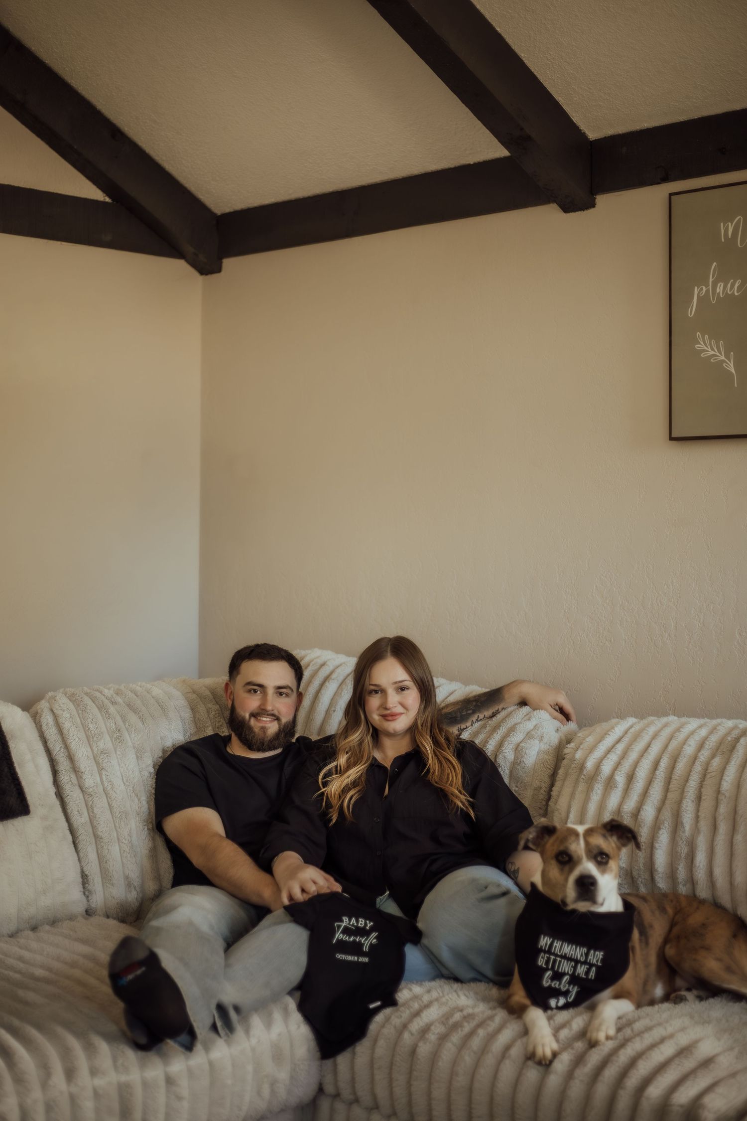 Couple in black outfits sitting on cozy couch with their brown dog during an in-home lifestyle photography session.