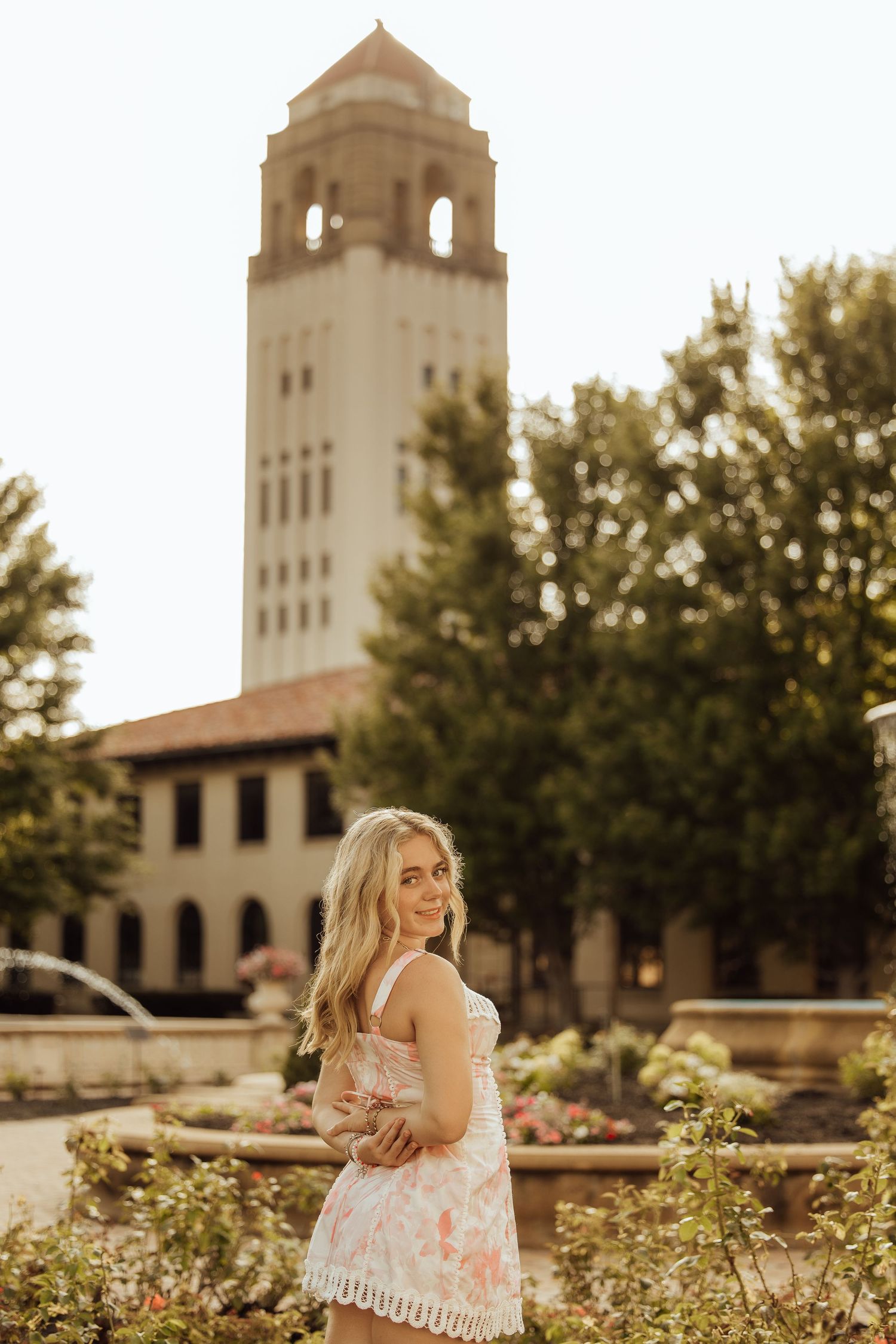 Young blonde woman in floral dress smiling outdoors near Hoover Tower at Stanford University campus.