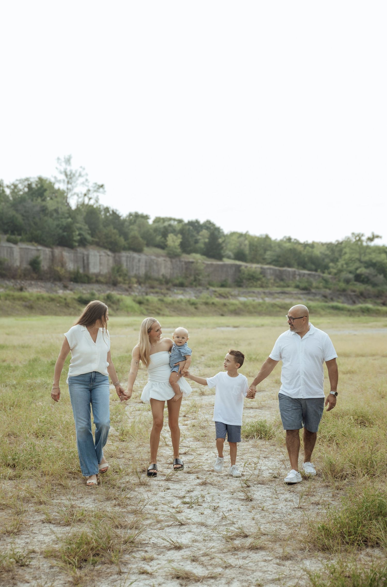 Happy family of five walking together hand-in-hand across a sunny open field.