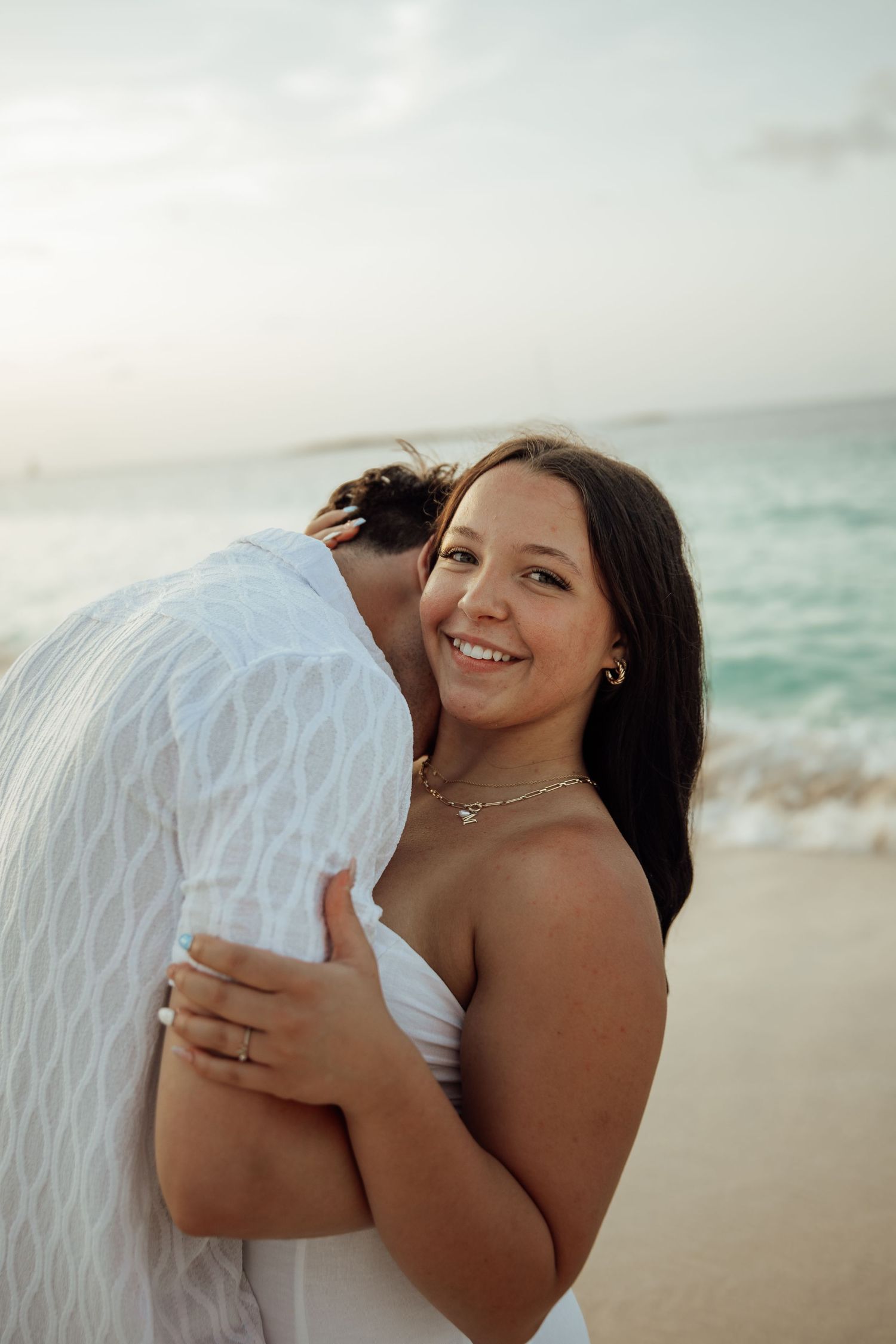 Man kissing woman on the cheek as she smiles at camera during a romantic beach photo session.