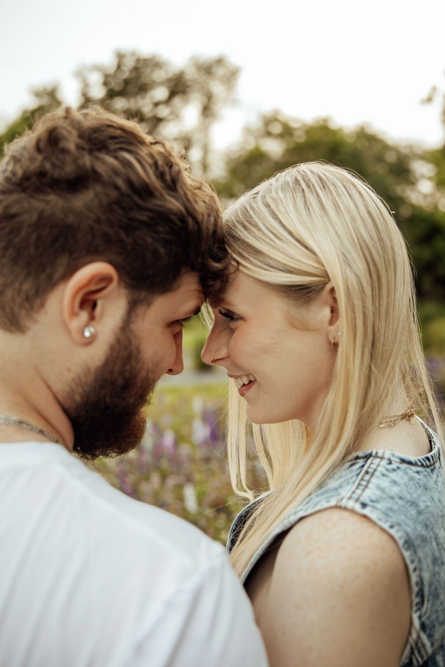 A couple smiles and touches foreheads romantically outdoors with colorful flowers in the background.