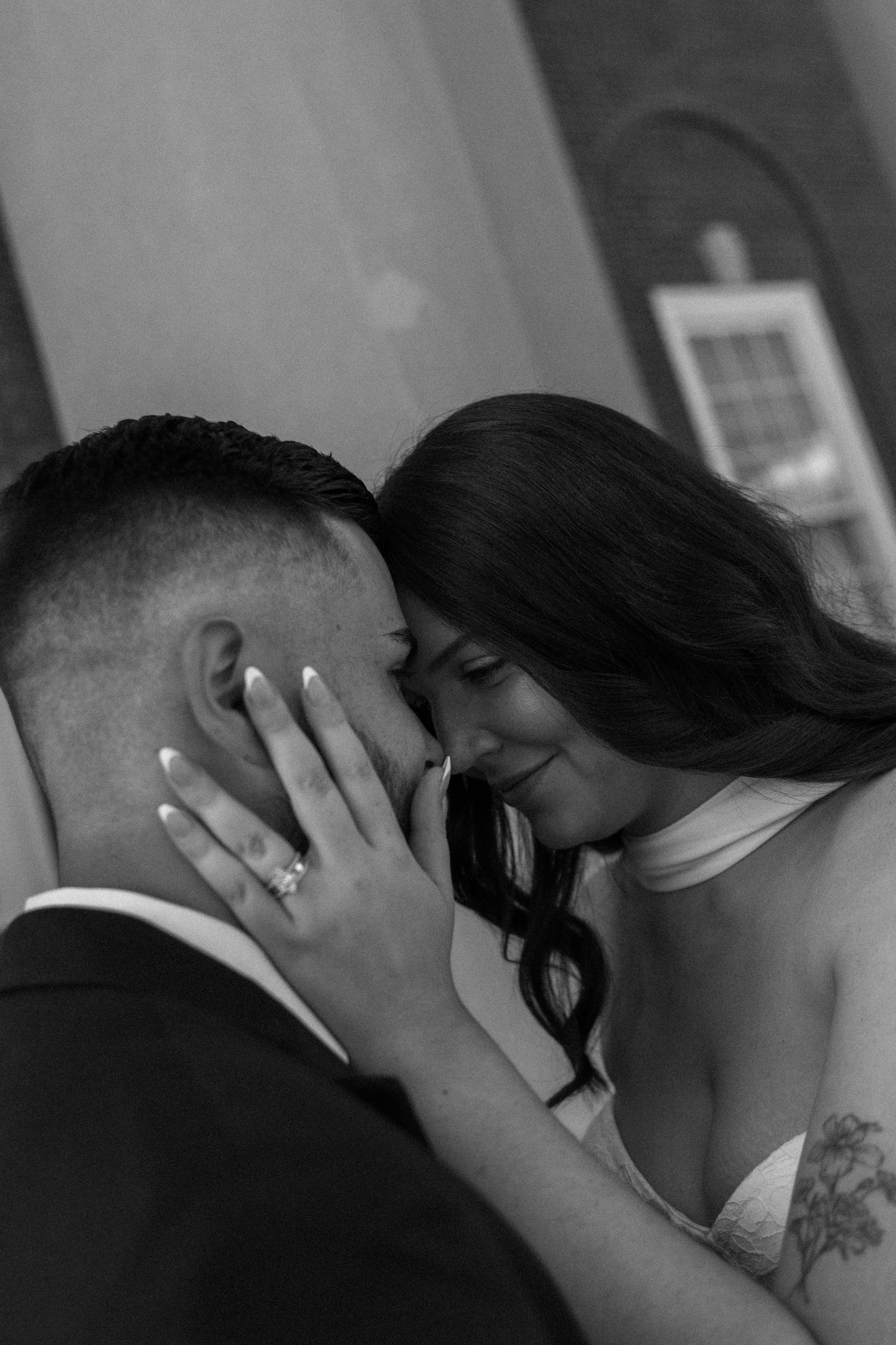 Black and white wedding photo of bride and groom sharing an intimate moment, bride showing diamond ring.