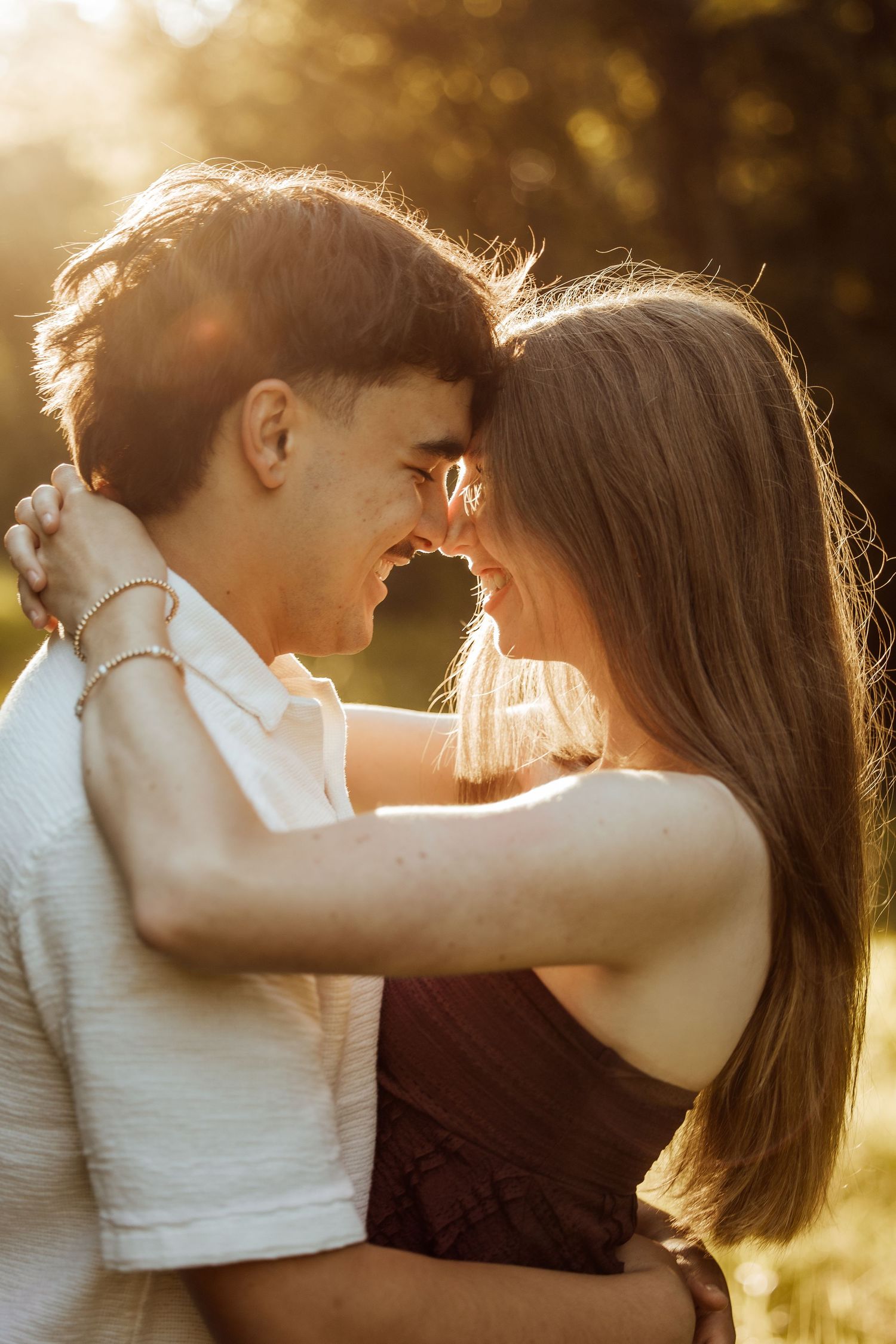 Couple sharing a romantic moment outdoors, touching foreheads and smiling in warm golden sunset light.