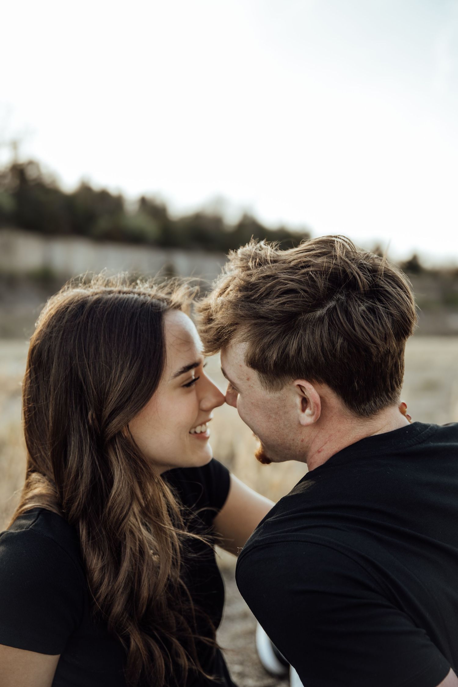 Couple in matching black outfits touching foreheads and smiling in an outdoor engagement photo session.