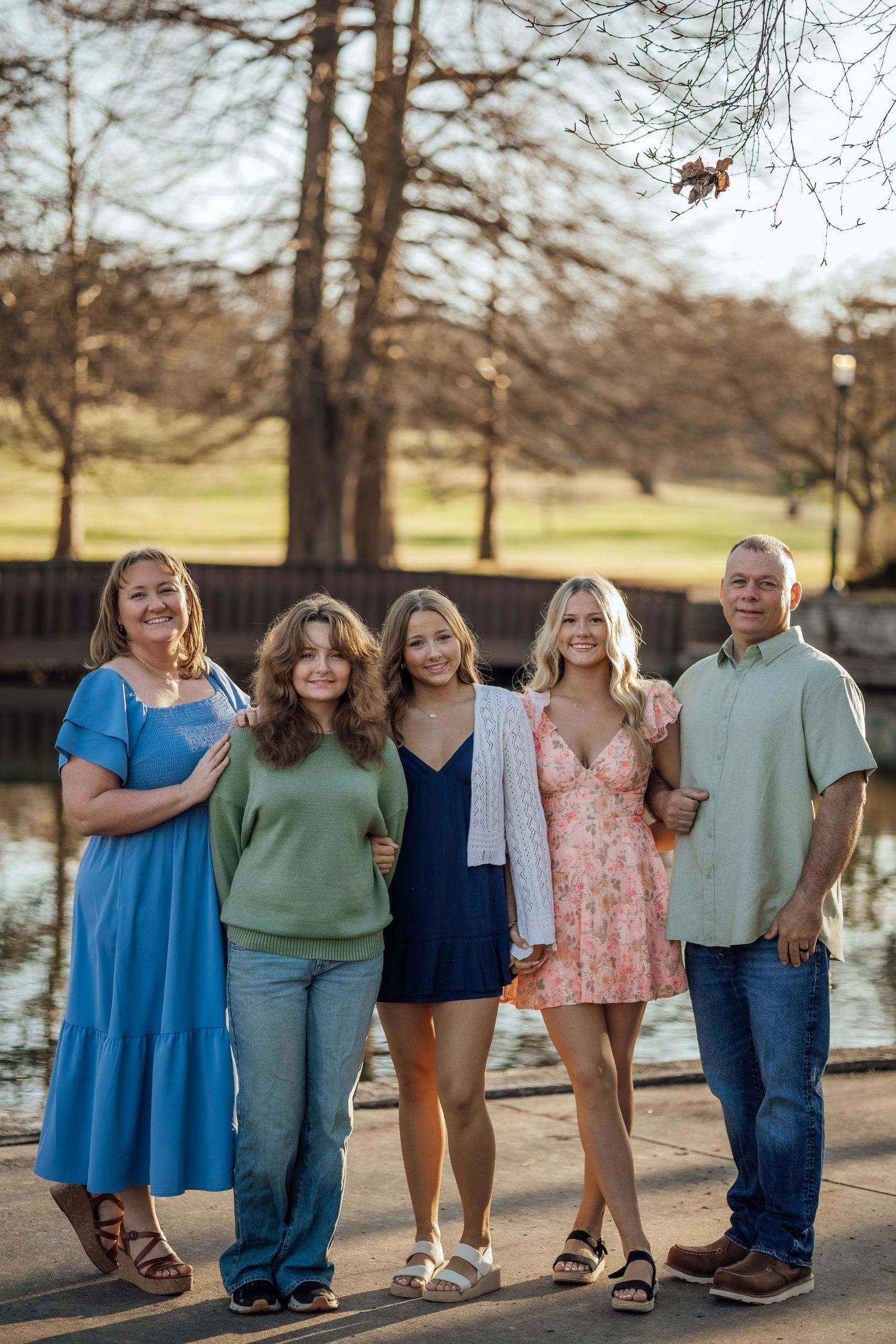 Family of five posing by a pond during a warm sunset outdoor family portrait session in the park.