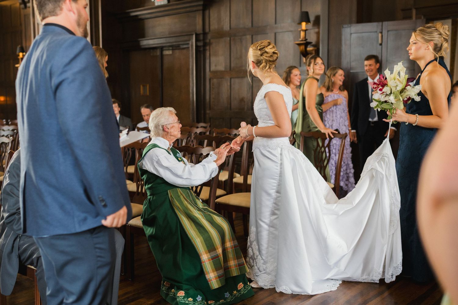 Bride in white gown holds hands with elderly woman in green dress at elegant wedding reception.