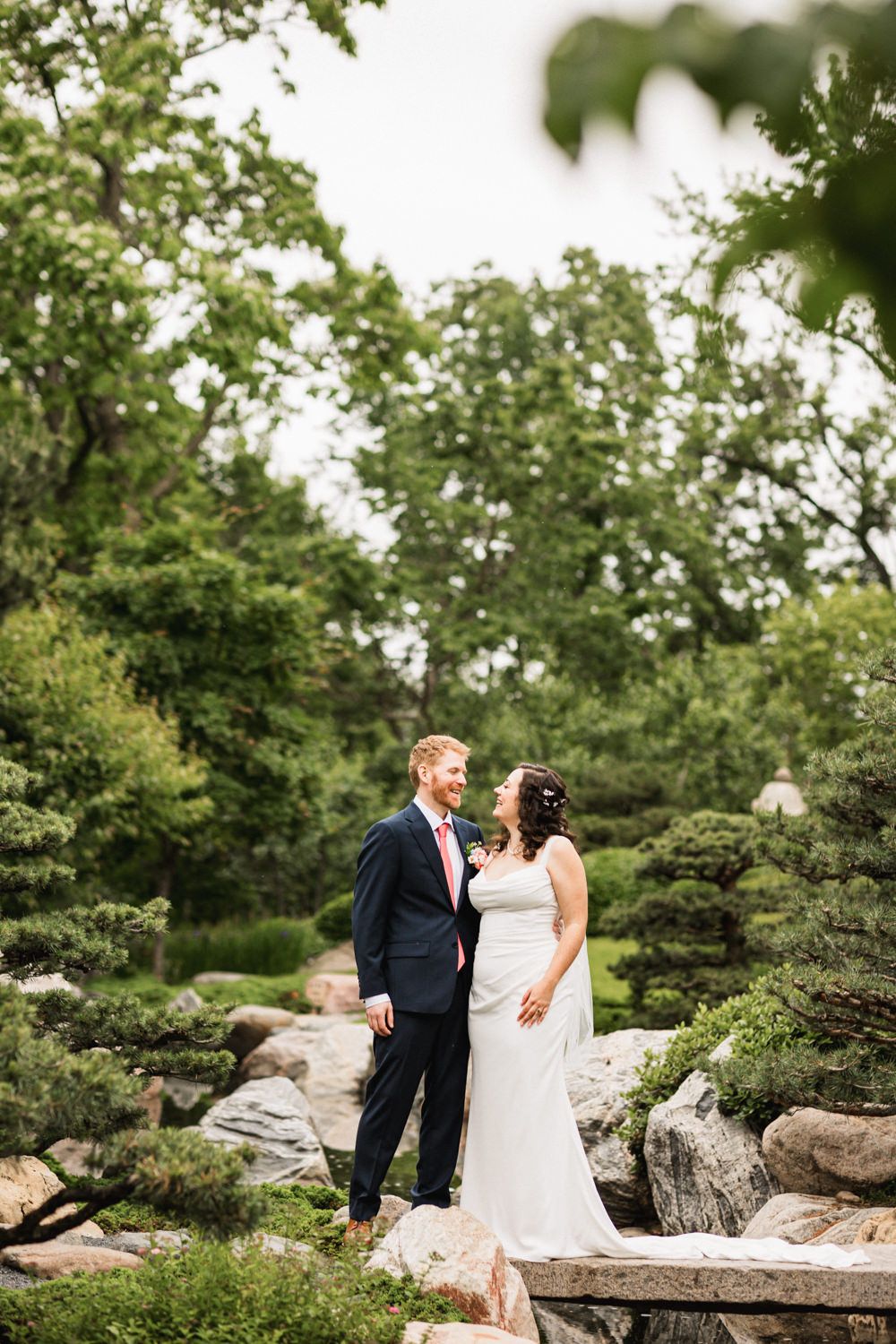 Natural outdoor wedding portraits among trees and rocks in a garden setting.
