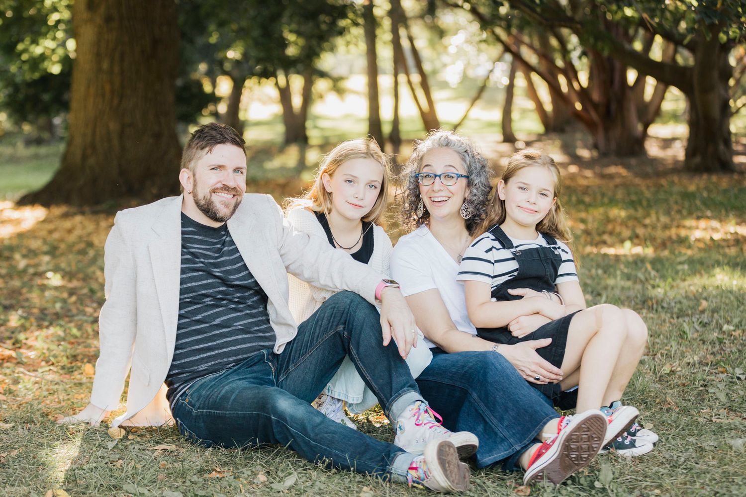 A relaxed family moment captured on grass with fallen autumn leaves in the background.