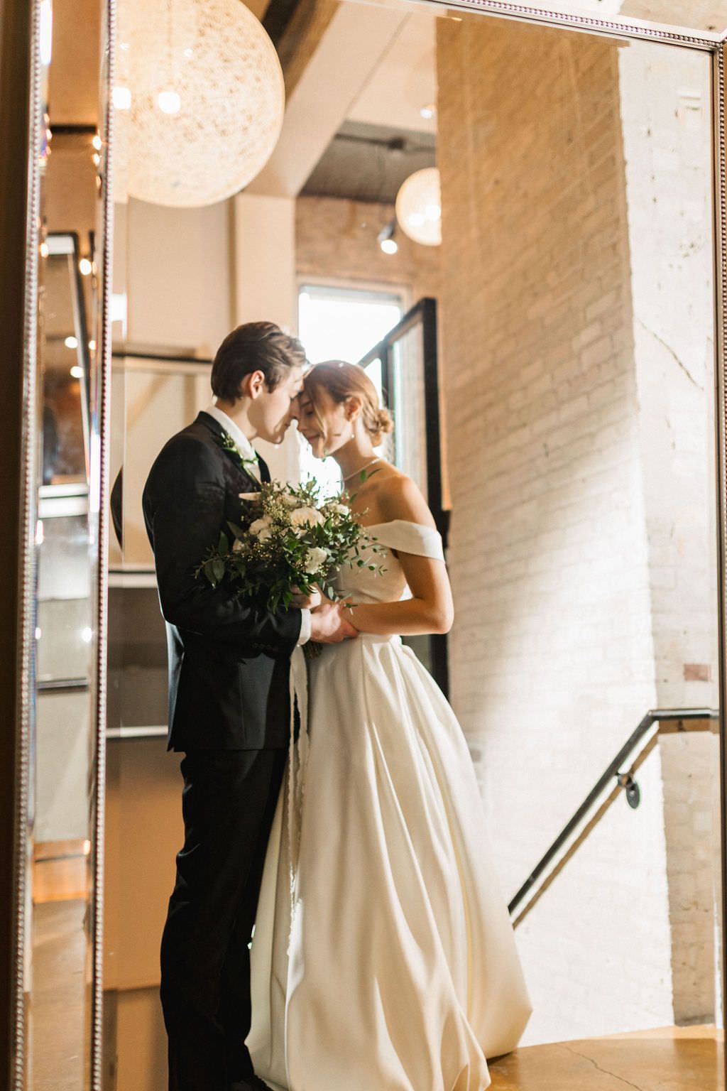 Wedding couple shares an intimate dance moment in a light-filled room with white brick walls.