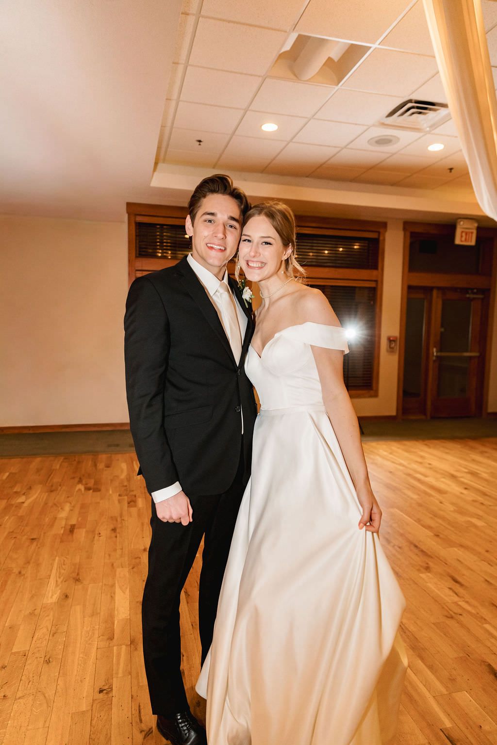 Wedding couple sharing a joyful moment while dancing in an elegant reception hall with hardwood floors.