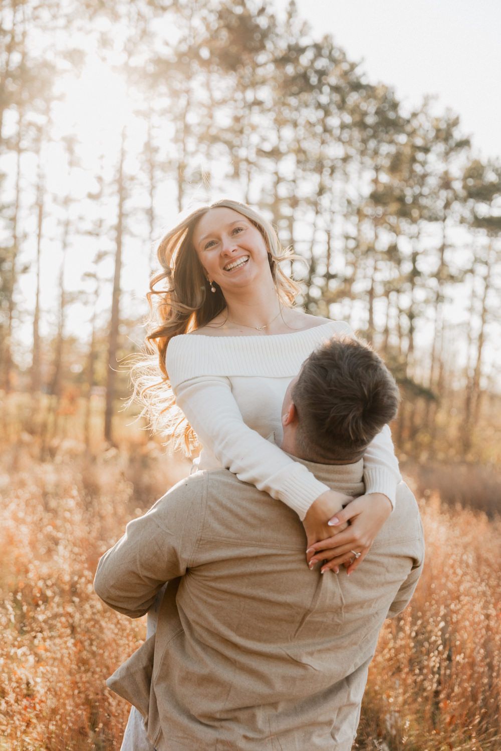 A playful couple laughs together in a natural setting with warm autumn colors.