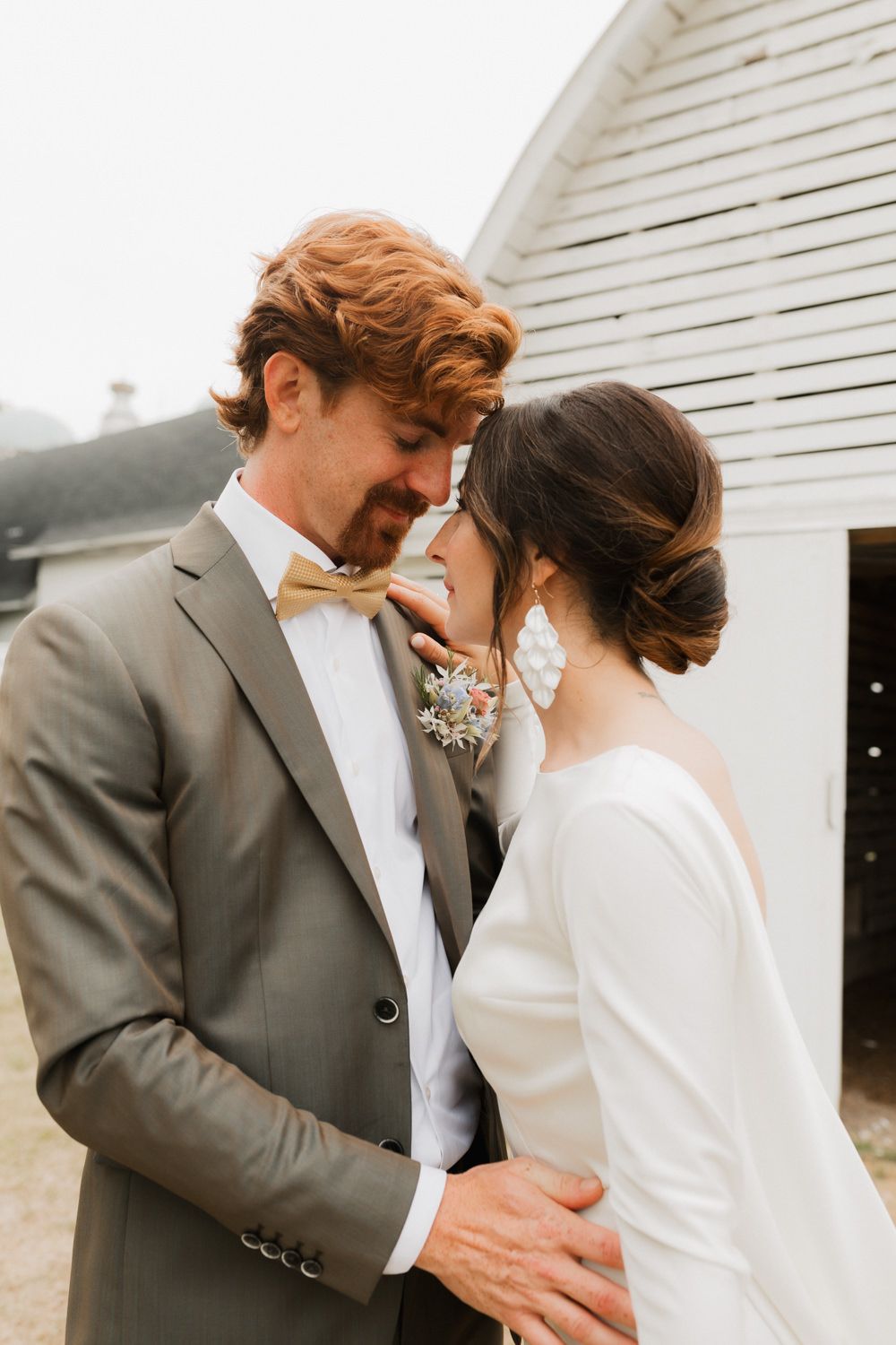 Romantic wedding couple in formal attire share intimate moments against white building exterior in photo series.