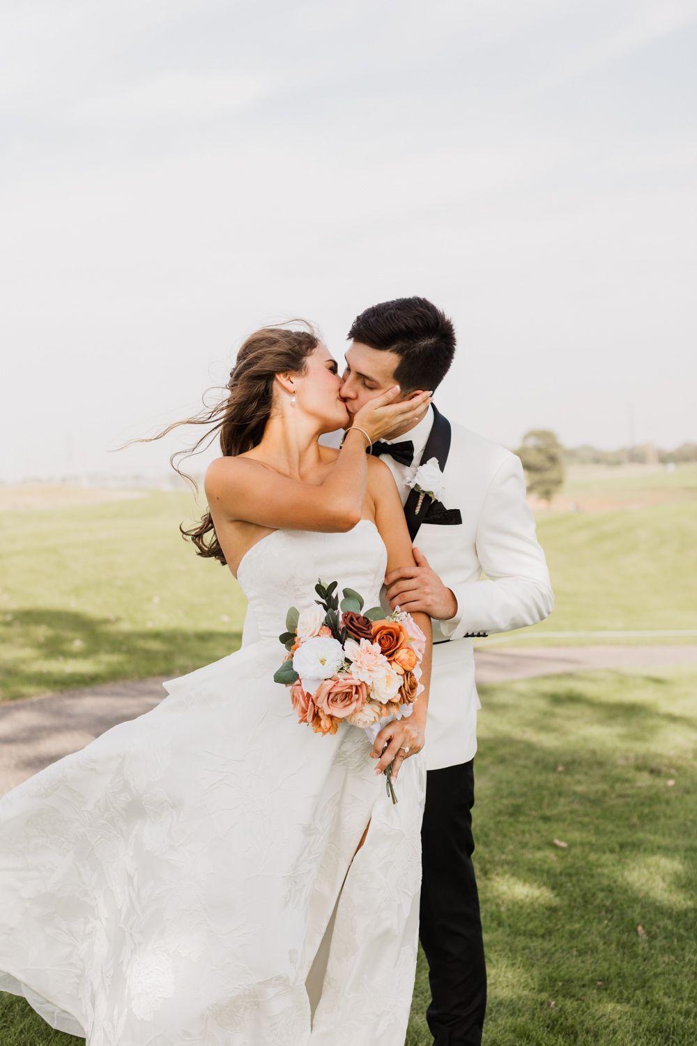 A romantic wedding couple embraces and kisses on a grassy hillside in a series of candid moments.