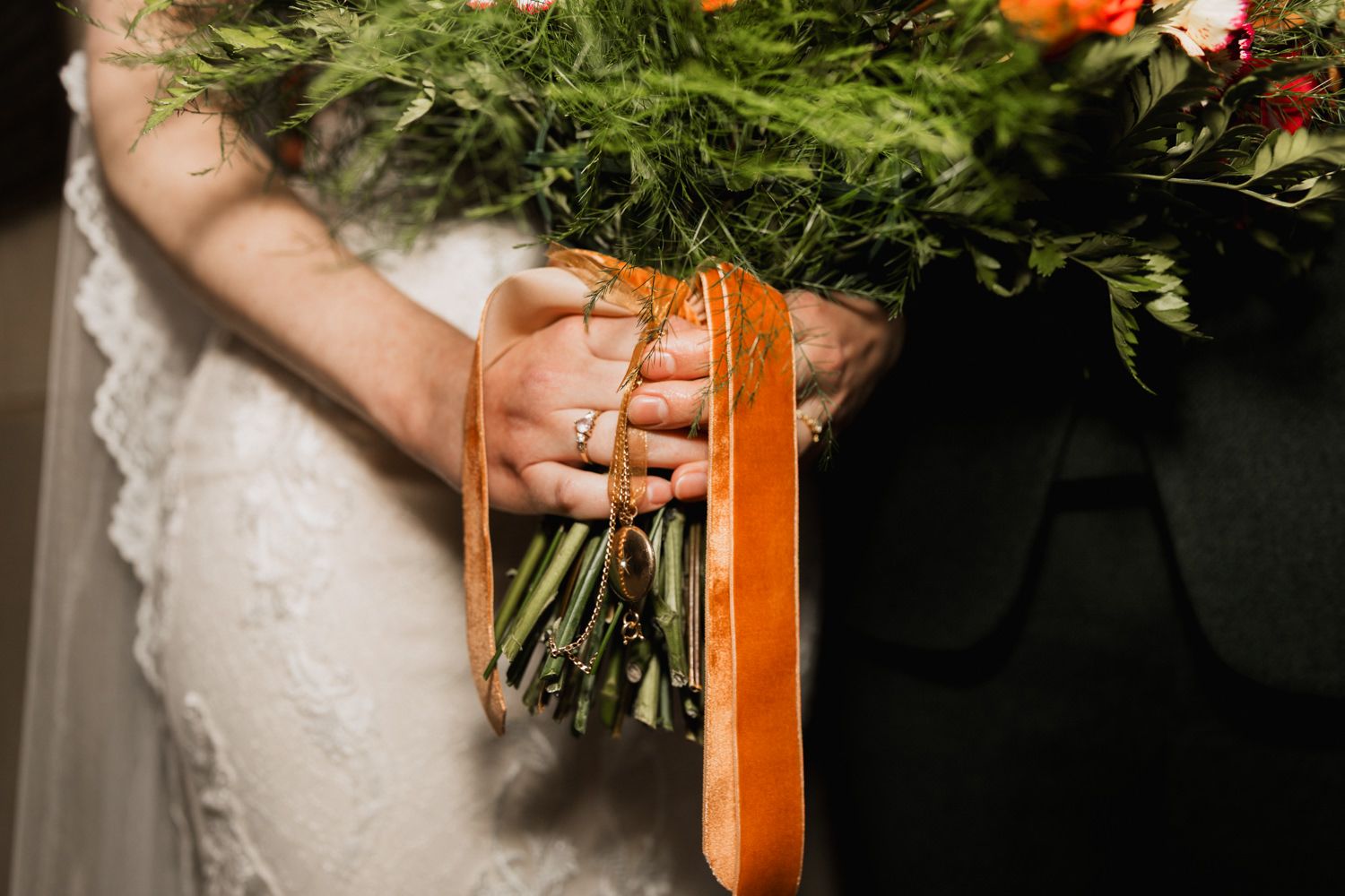 Close-up details of orange floral bouquet with greenery and ribbons at a wedding.