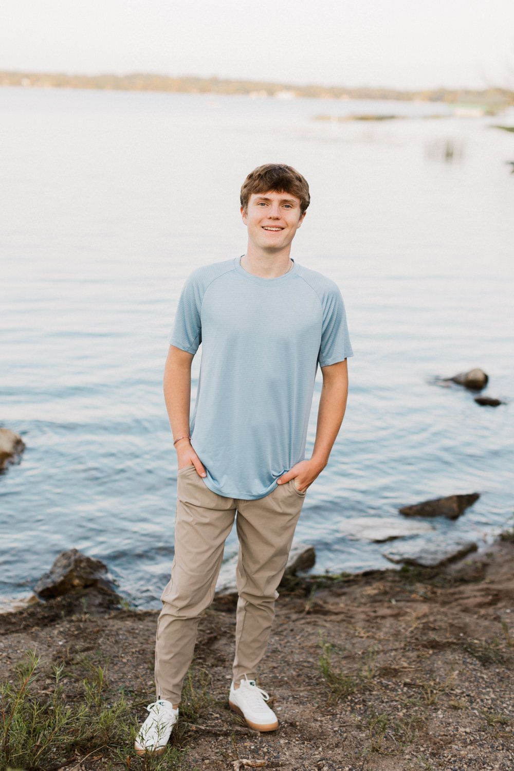 Person in light blue shirt and khaki pants standing on rocky waterfront.