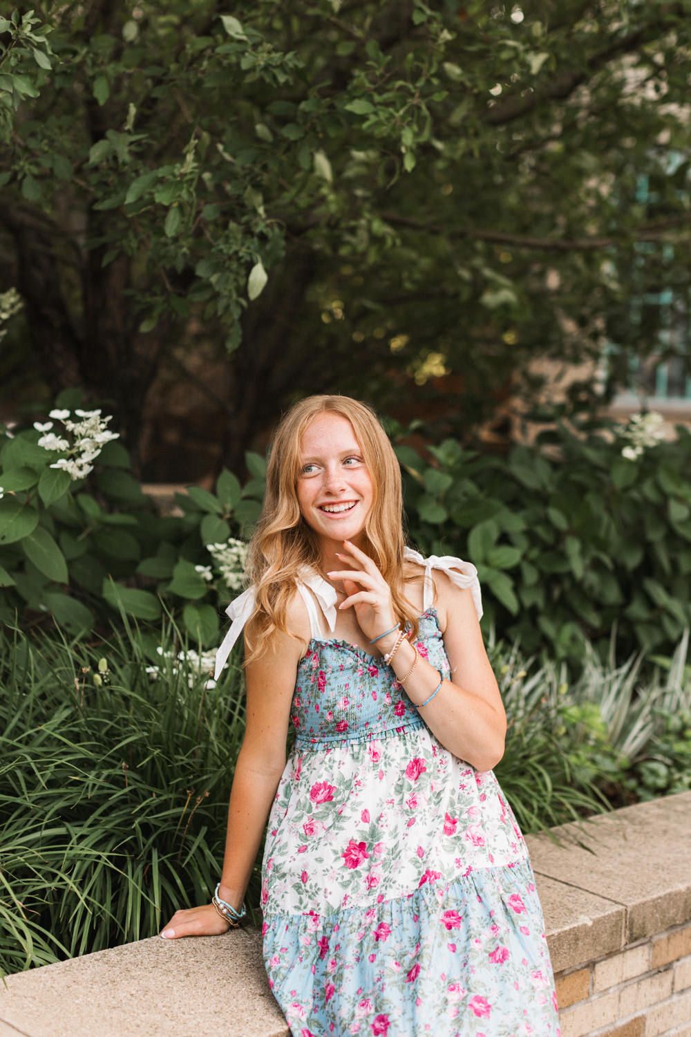 Floral sundress in blue and pink patterns adds a cheerful touch to a summer garden setting with brick walls and greenery.
