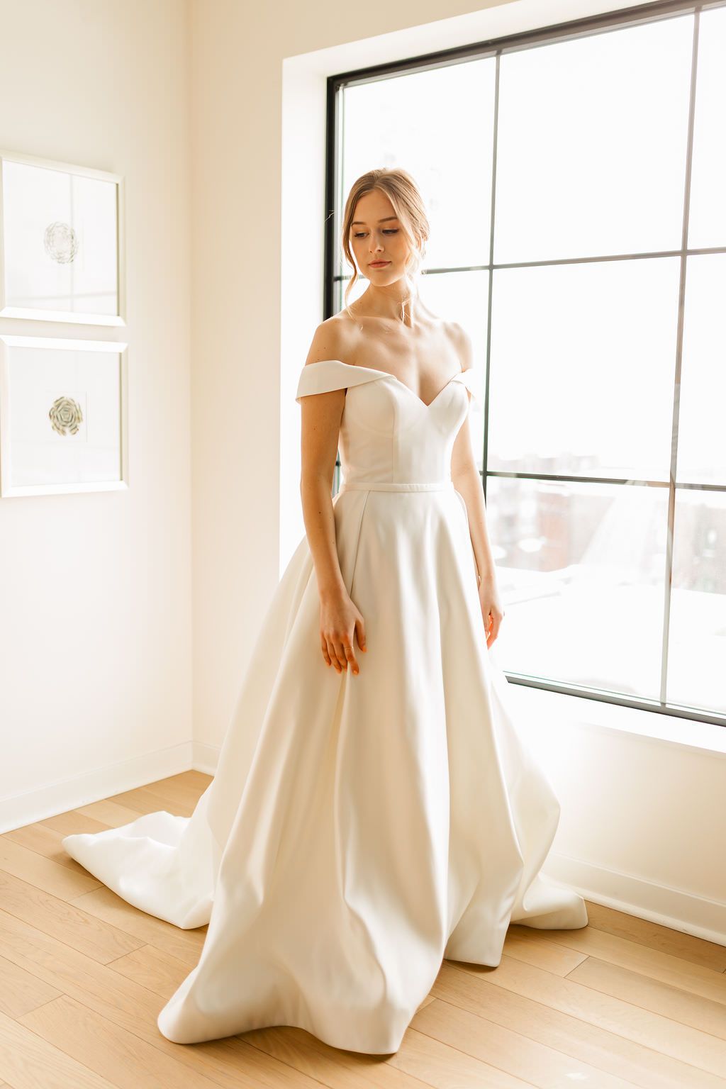 Elegant bride in a modern off-shoulder wedding gown photographed in a bright indoor space.