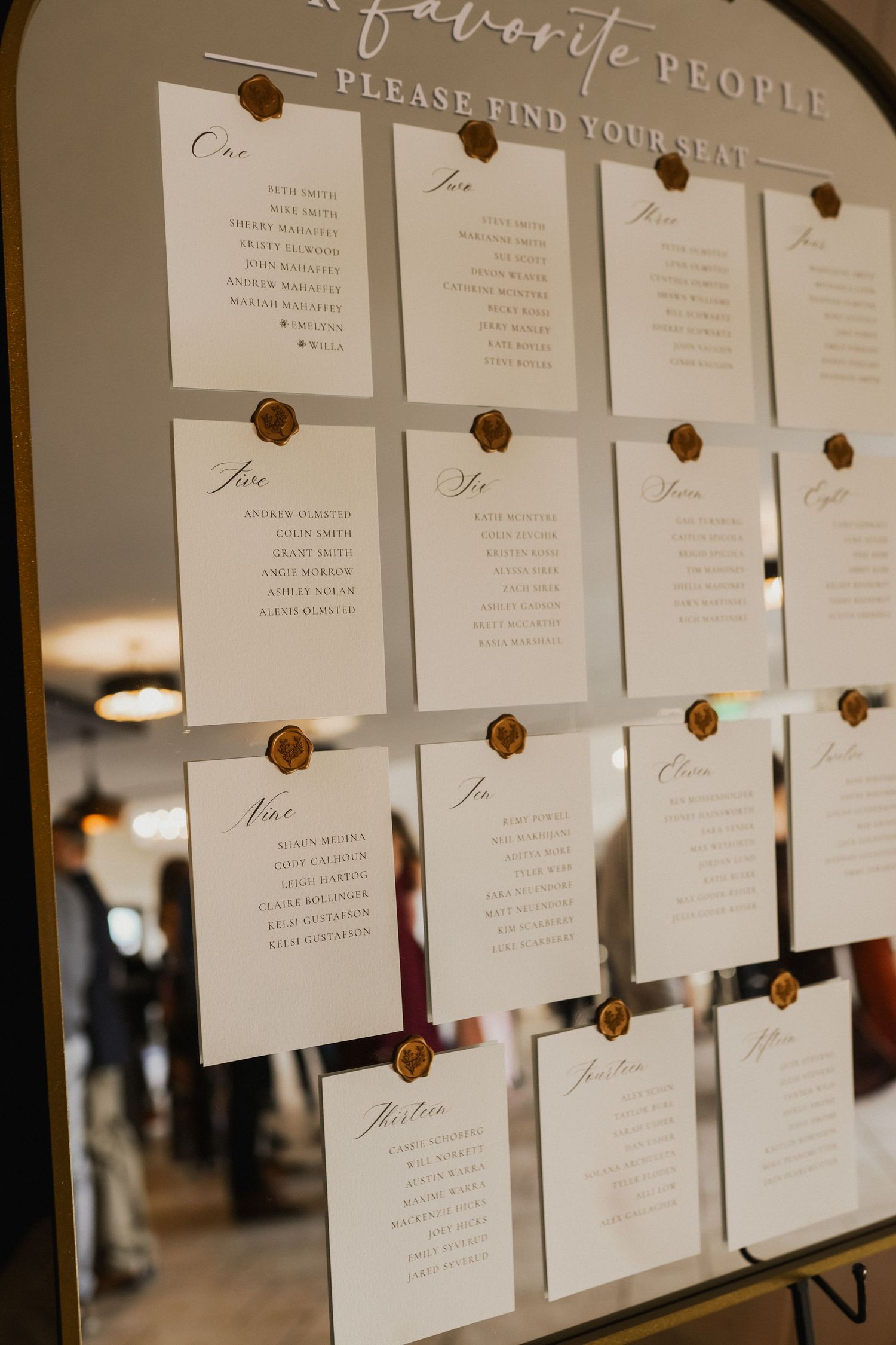 Wedding seating chart on a mirror with names on cards sealed with wax, reading please find your seat.