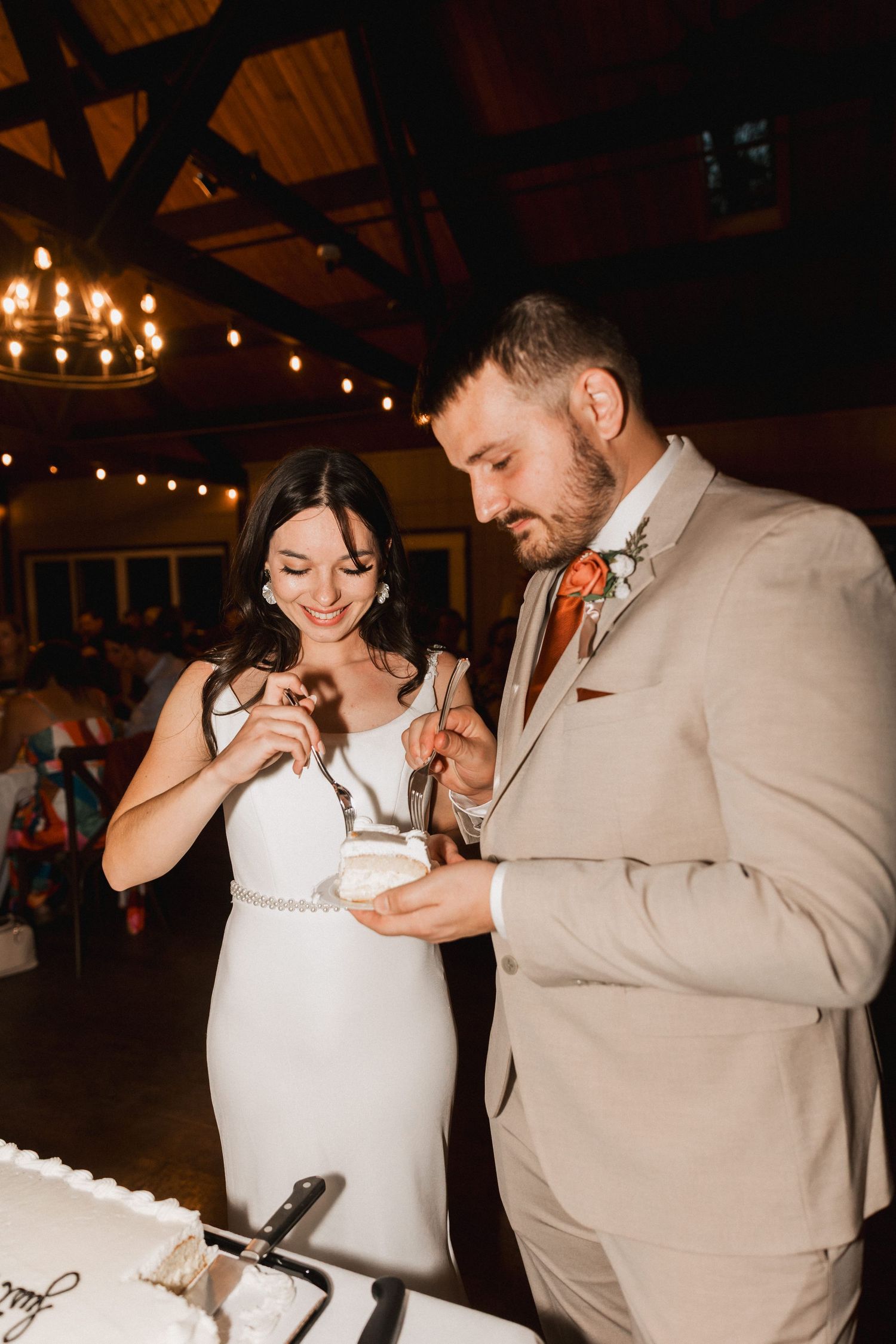 A couple playfully smashes cake on each others faces during their wedding reception in a rustic venue.