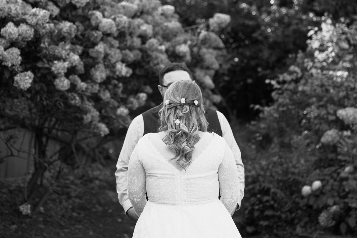 A romantic black and white wedding photo with a couple embracing in a garden surrounded by blooming flowers.