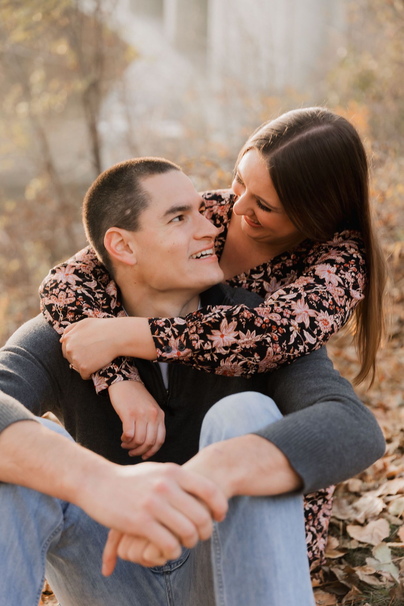 Couple sharing a tender moment outdoors in autumn, woman embracing man from behind among fallen leaves.