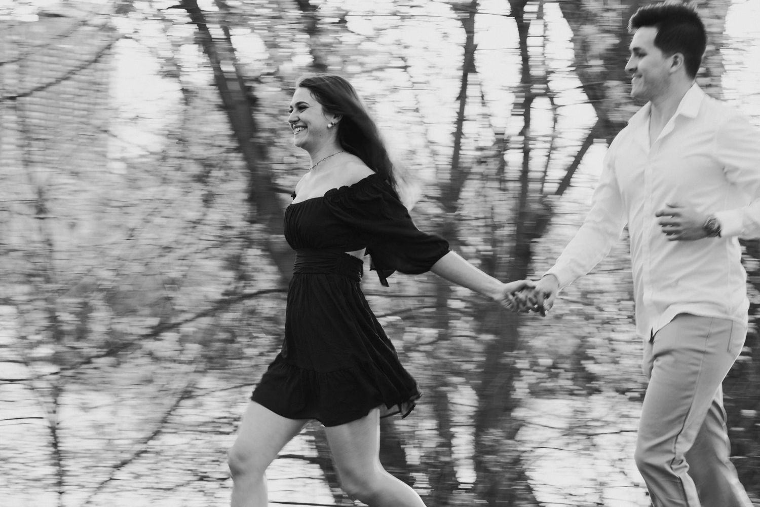 A couple runs and laughs together holding hands outdoors in a black and white photo.